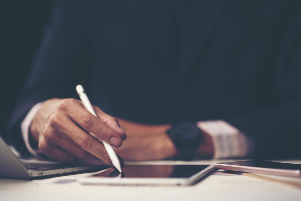 A person in a suit writing an e-signature using a stylus on an electronic tablet