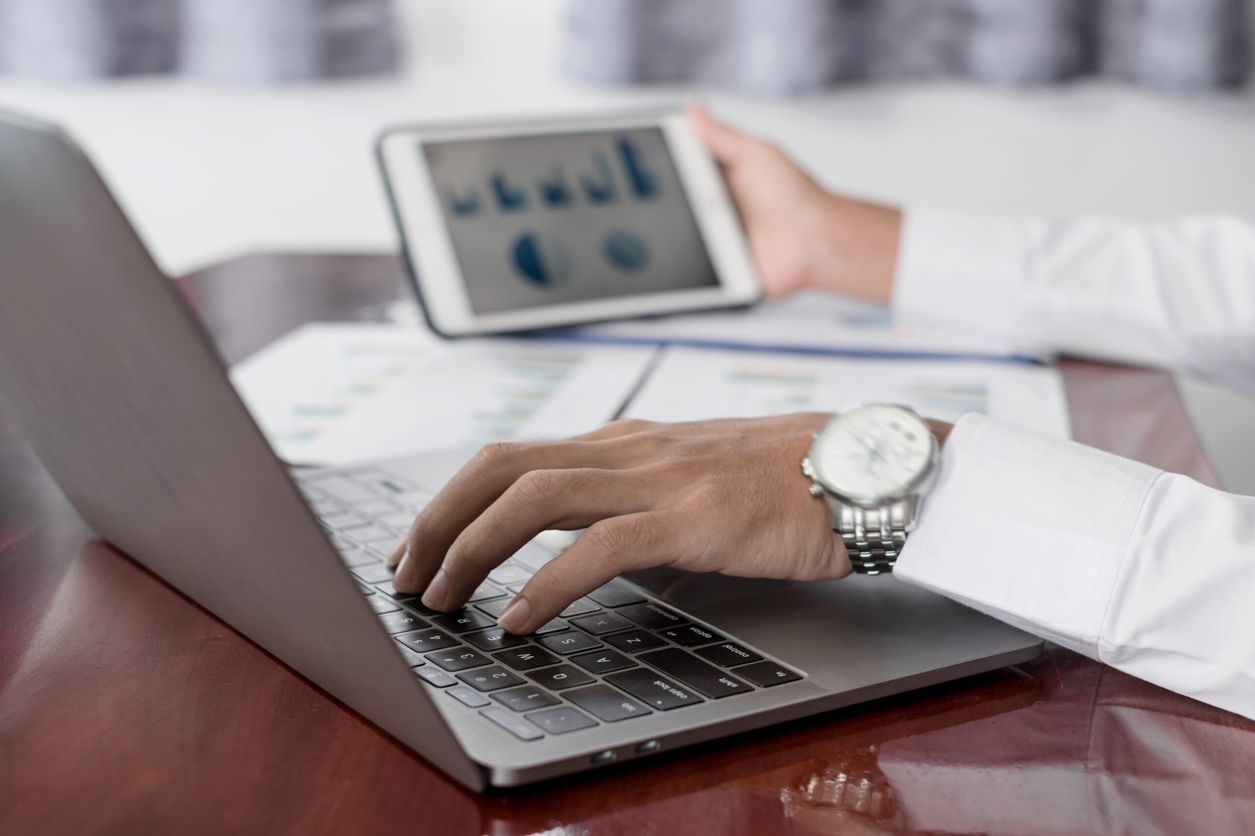 A person’s left hand on a laptop keyboard and the right hand holding an electronic tablet