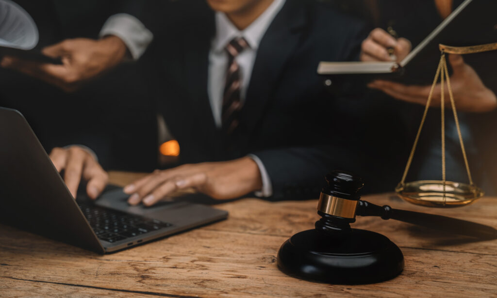 Lawyers collaborating at a desk with a laptop, a gavel, and scales of justice